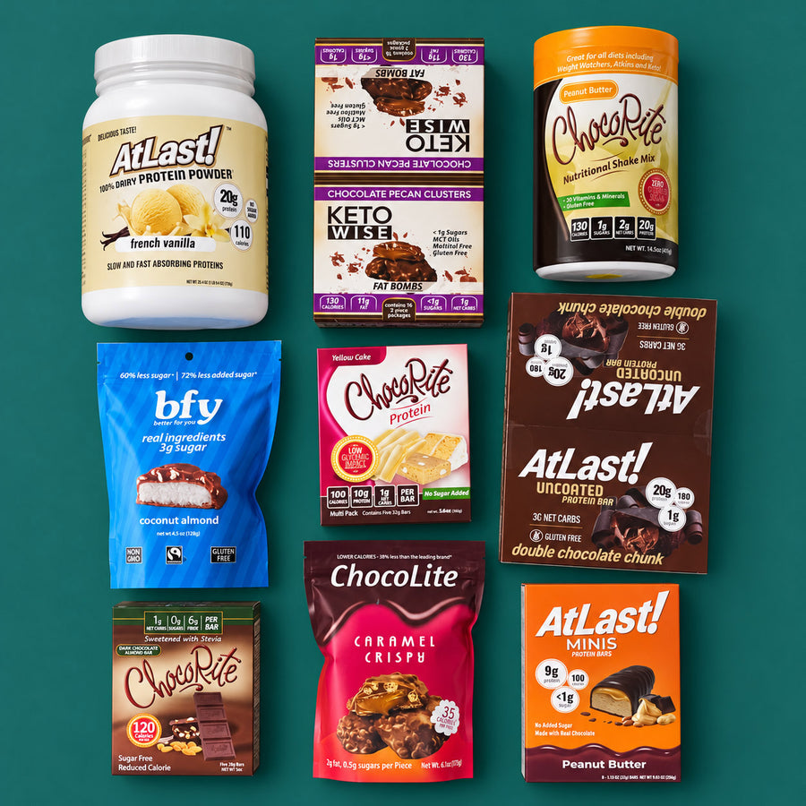 Nine HealthSmart products on a teal surface: AtLast! protein powder, Keto Wise Fat Bombs pecan clusters, ChocoRite shake mix, bfy coconut almond, ChocoRite Yellow Cake protein bars, AtLast! Double Chocolate Chunk protein bars, ChocoRite dark chocolate almond bars, ChocoLite Caramel Crispy and AtLast! Minis Peanut Butter.